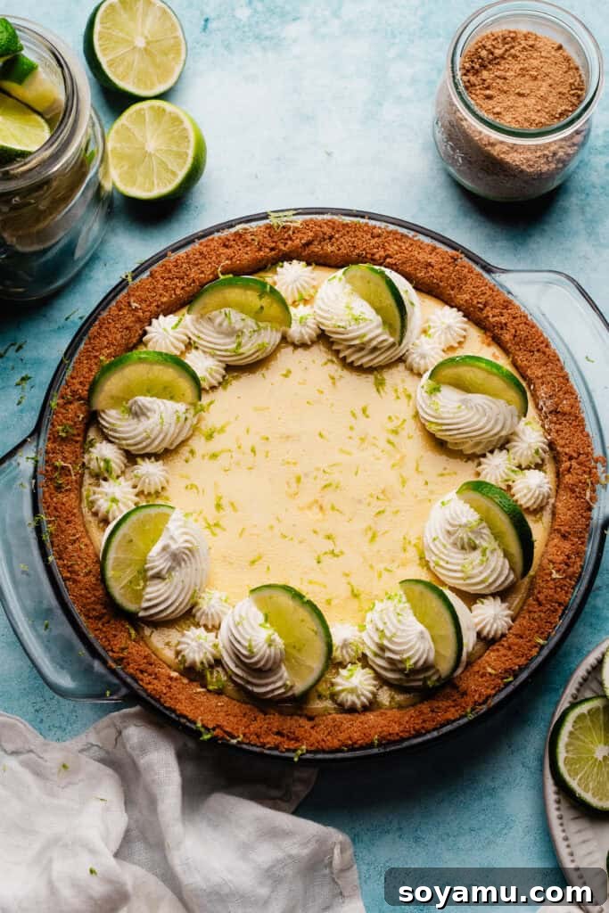 Ultra-Creamy Key Lime Pie Recipe for Perfectly Tangy Slices 12 The baked, chilled pie on a blue surface, decorated with swirls of whipped cream and lime slices.