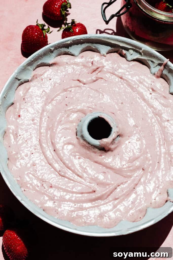 Pink cake batter poured into a bundt pan, ready to be baked.