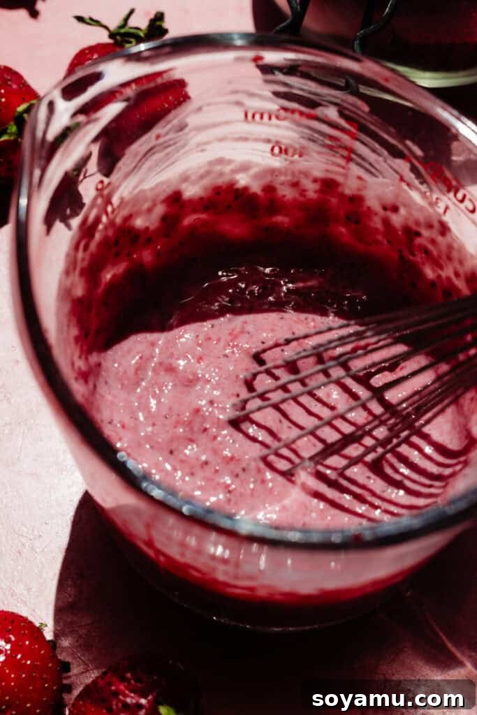 A measuring cup filled with the thick, pink strawberry milk liquid.