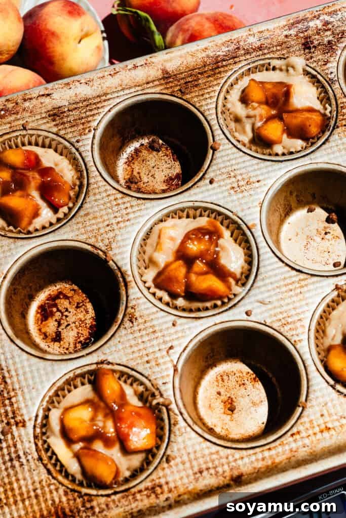 Southern-Style Peach Cobbler Muffins Recipe 11 Batter in the muffin tin, with peach cobbler topping added on top.