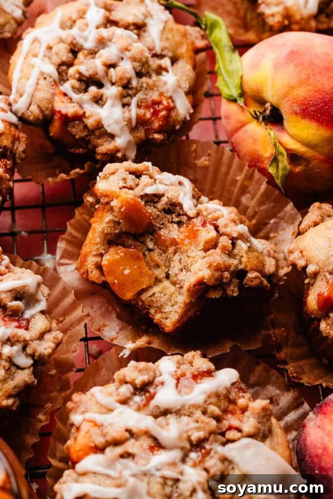 Southern-Style Peach Cobbler Muffins Recipe 15 A close-up on a peach muffin on a wire rack, surrounded by other muffins. It has a bite missing, showing the fluffy texture inside.