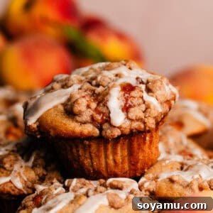 Southern-Style Peach Cobbler Muffins Recipe 20 A close-up on a peach cobbler muffin drizzled with vanilla glaze, stacked on top of other peach cobbler muffins.
