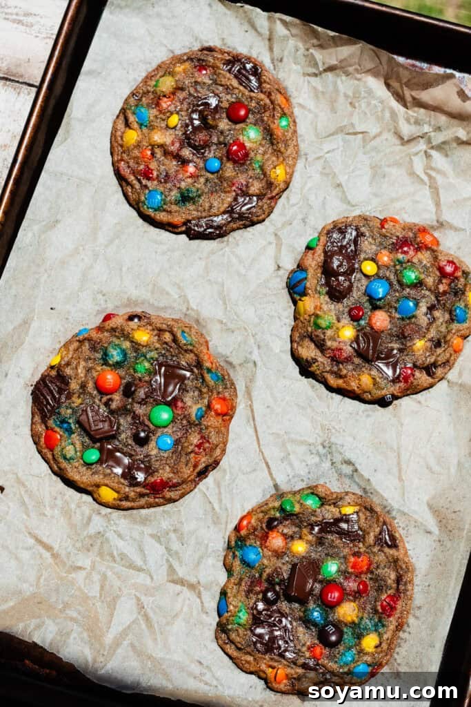 Thin, Chewy M&M Chocolate Chip Cookies 11 A bird's eye view of four baked cookies on a cookie sheet.