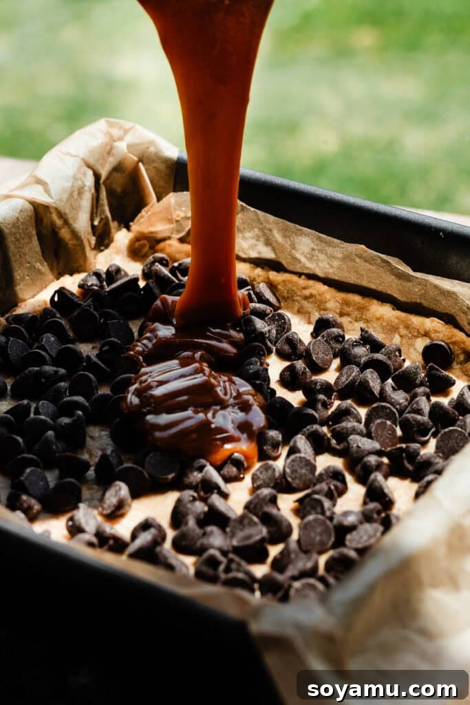 Carmelita Bars with Homemade Salted Caramel Filling 9 Salted caramel sauce being poured over the chocolate chips in the pan.