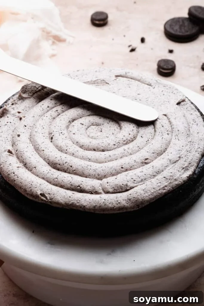 Decadent Moist Oreo Cake Recipe 12 An offset spatula smoothing a layer of piped frosting over a cake layer.