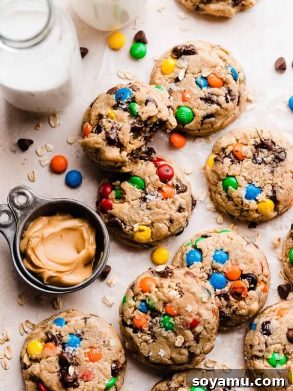 Monster cookies on a light surface, with a bowl of peanut butter and glasses of milk.