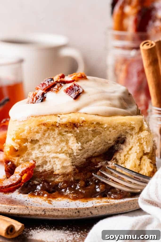 A close-up of a maple bacon cinnamon roll on a plate, with the visible maple caramel sauce on bottom.