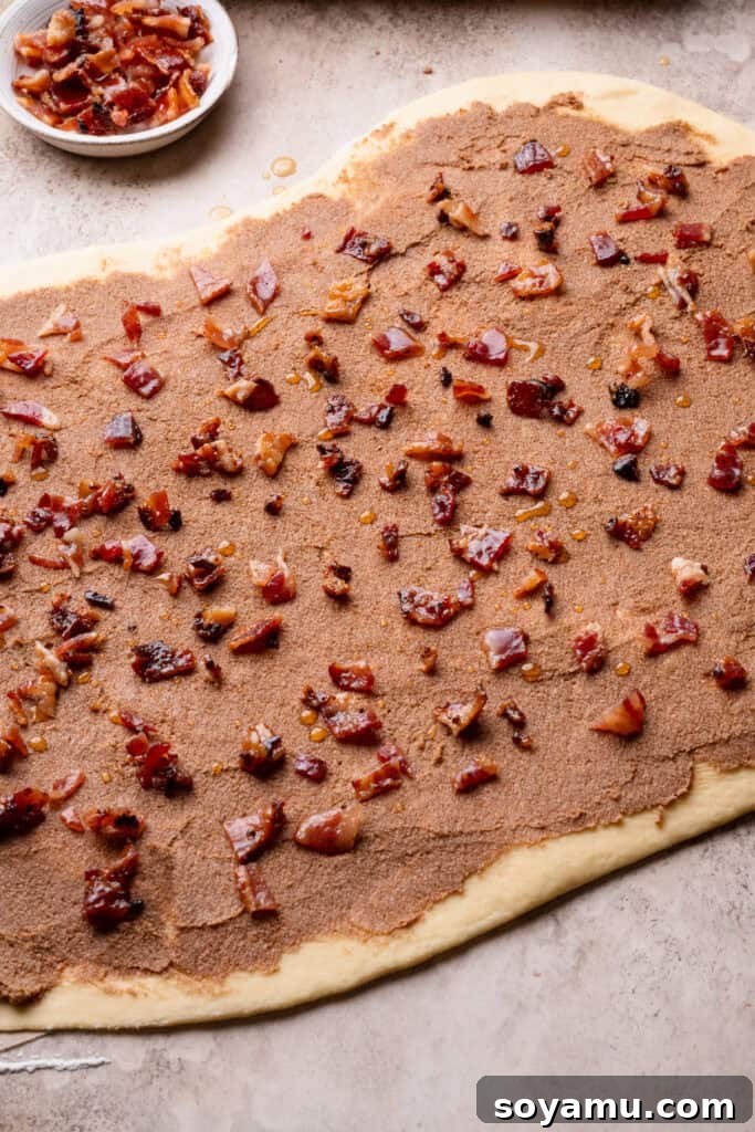 The dough rolled out and topped with the cinnamon filling, maple syrup, and bacon pieces.