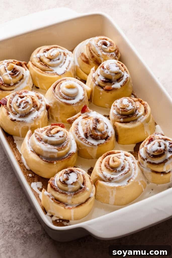 The risen rolls in a baking dish, drizzled with heavy cream.