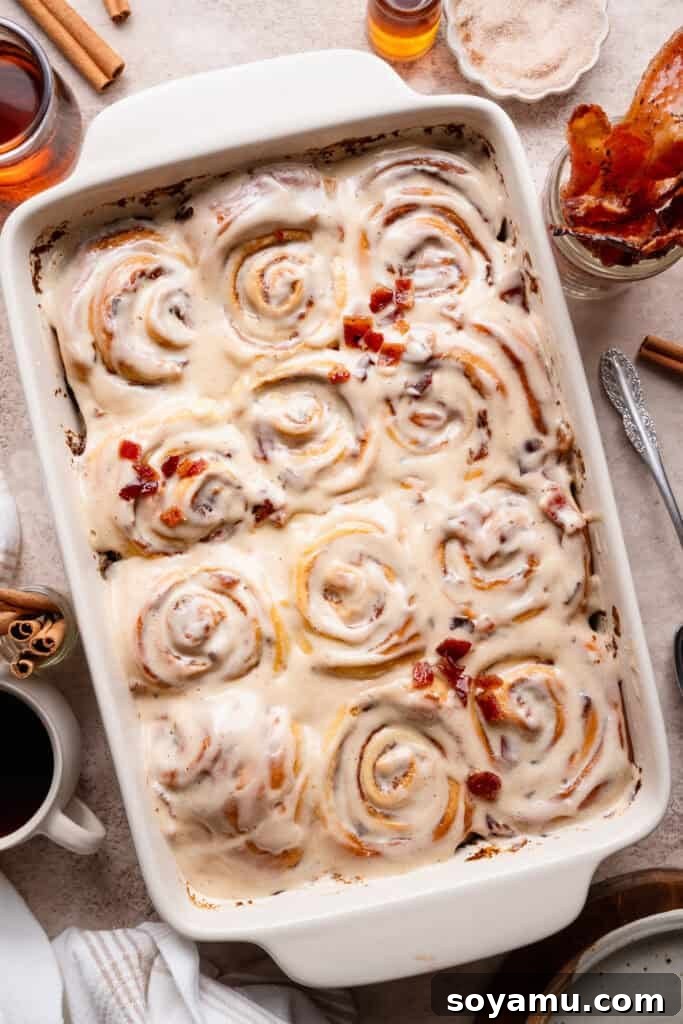 A bird's eye view of the pan of baked maple bacon cinnamon rolls, topped with maple cream cheese icing and candied bacon pieces.